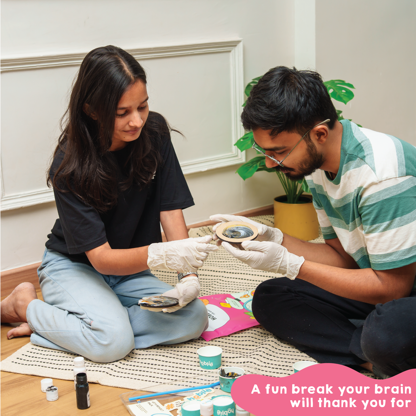 Two people sitting on the floor with fluid art coaster painting kit, doing a creative activity to give brain a fun break